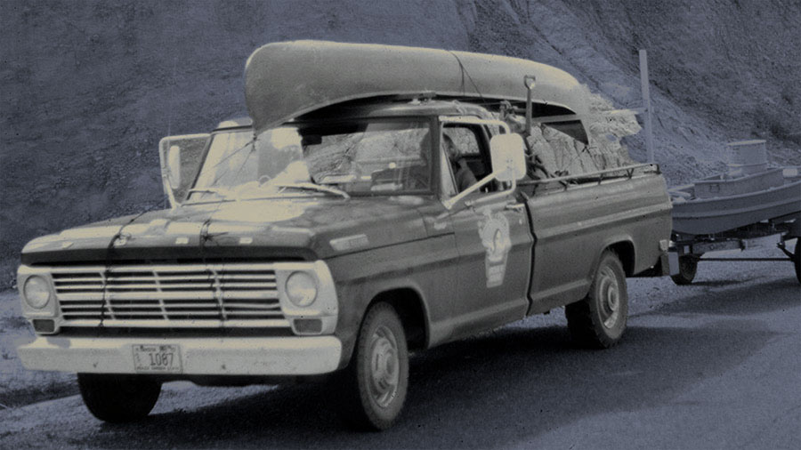 Photo of old GNF truck with a canoe on top and pulling a boat