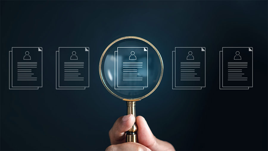 Abstract of job applications with a hand holding a magnifying glass over one