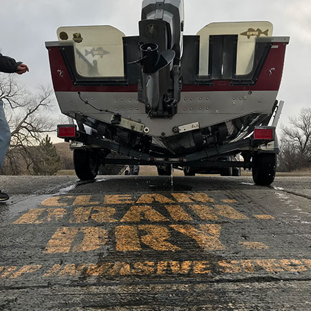 Boat being drained on ramp above painted words Clean, Drain, Dry