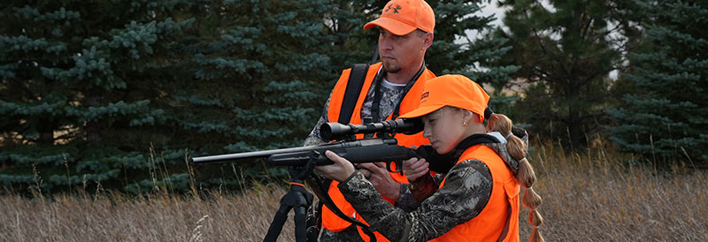 Father watching as daughter sites gun towards deer